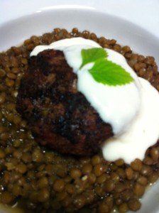 Grilled Lamb Burger and Minty Yogurt Sauce over Lentils with a Mint Leaf Garnish (Photo Credit: Adroit Ideals)