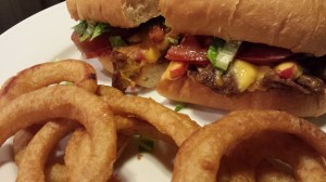 Cheesesteak sandwich with grilled onions, red bell peppers, American cheese, lettuce and tomato.  Side of onion rings.  (Photo Credit: Adroit Ideals)