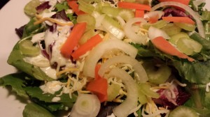 Add the shredded cheese, carrots, celery, and sweet onion to the dressed greens (Photo Credit: Adroit Ideals)
