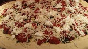 Ready for the oven: Pesto, roasted tomatoes, sliced garlic, ricotta, and mozzarella on a pizza dough (Photo Credit: Adroit Ideals)
