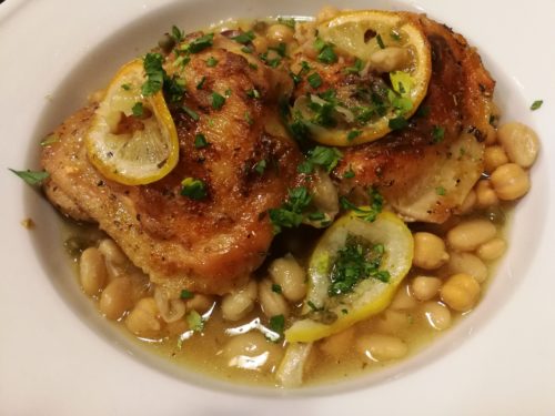 Two baked chicken thighs over white bean stew